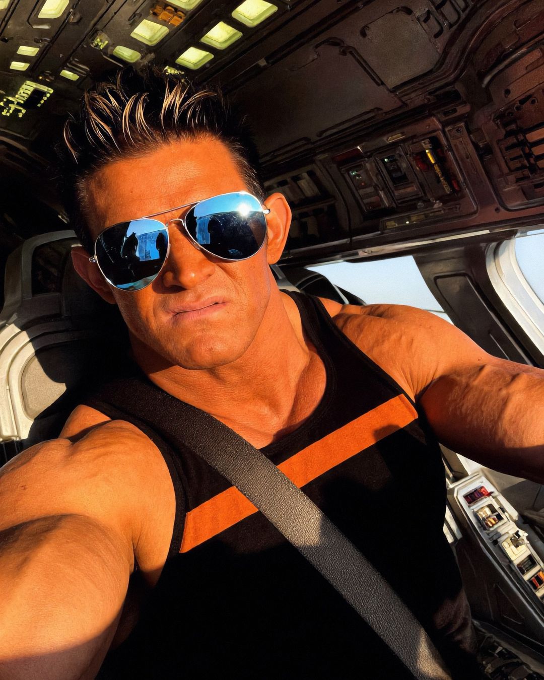 Elon Muskle in mirrored aviator sunglasses taking a selfie in a cockpit